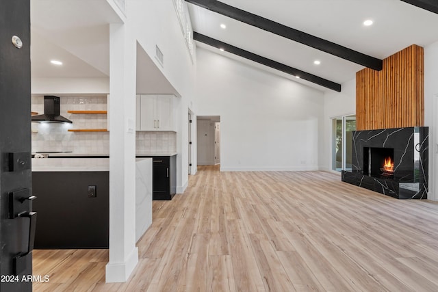 unfurnished living room with a high end fireplace, beam ceiling, light wood-type flooring, and high vaulted ceiling