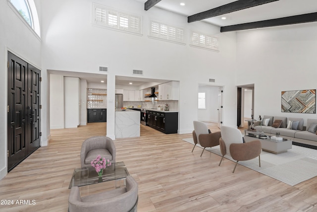 living room featuring a towering ceiling, a wealth of natural light, light hardwood / wood-style floors, and beam ceiling