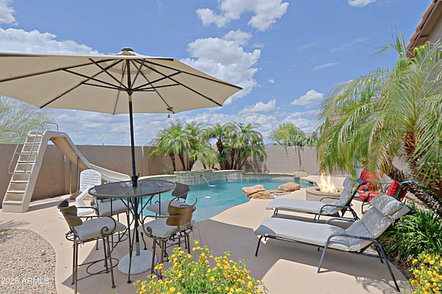 view of swimming pool featuring a water slide, a fire pit, a patio, and a fenced backyard