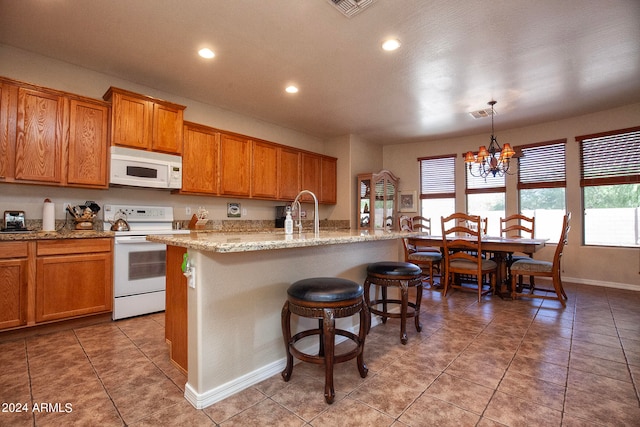 kitchen featuring decorative light fixtures, light stone countertops, a chandelier, a kitchen island with sink, and white appliances