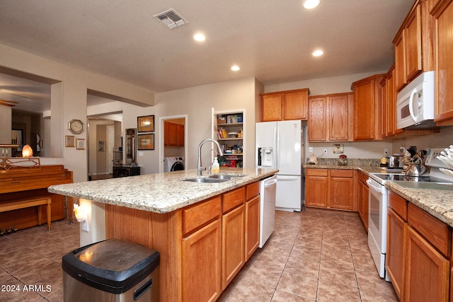 kitchen with light tile patterned floors, light stone counters, white appliances, and an island with sink