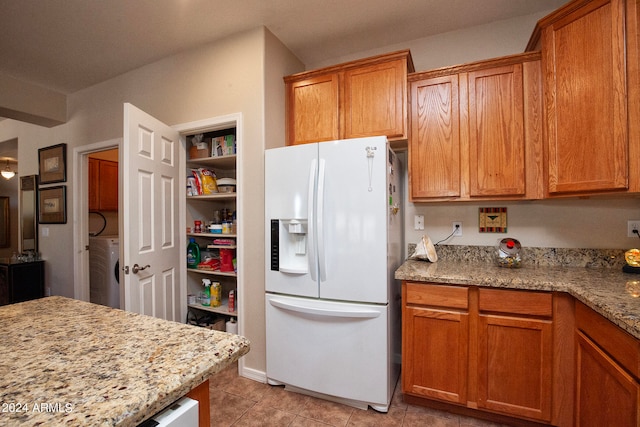 kitchen featuring white fridge with ice dispenser, light tile patterned floors, washer / clothes dryer, and light stone countertops