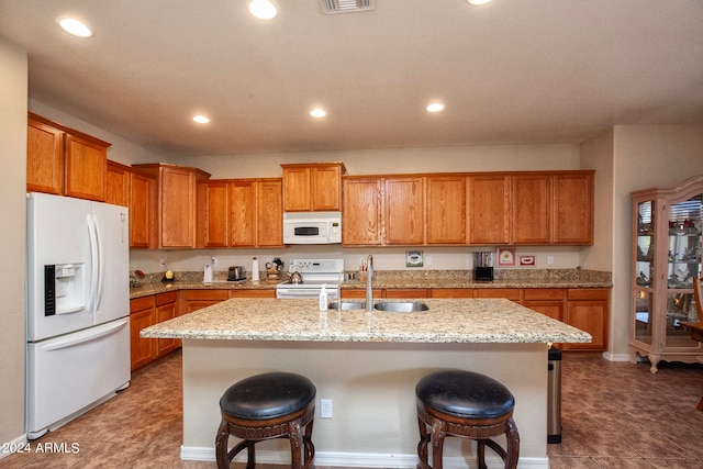 kitchen featuring a kitchen island with sink, light stone counters, and white appliances