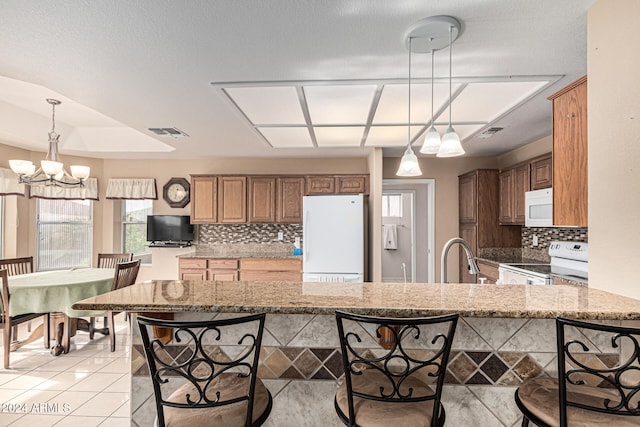 kitchen featuring kitchen peninsula, light stone countertops, and white appliances