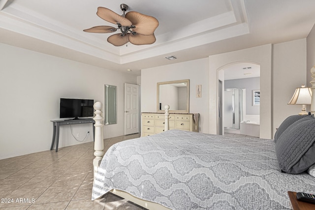 bedroom featuring light tile patterned floors, a tray ceiling, ensuite bath, and ceiling fan