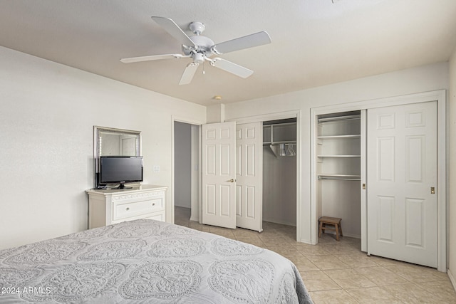 bedroom featuring ceiling fan, light tile patterned floors, and multiple closets