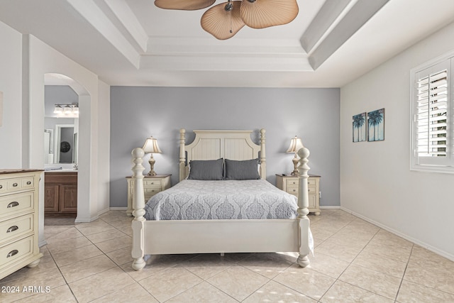 bedroom featuring ceiling fan, a raised ceiling, light tile patterned floors, and ensuite bath