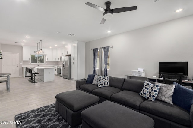 living room with ceiling fan, light wood-type flooring, and sink