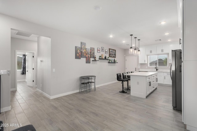 kitchen with a breakfast bar, a center island, stainless steel fridge, decorative light fixtures, and white cabinetry