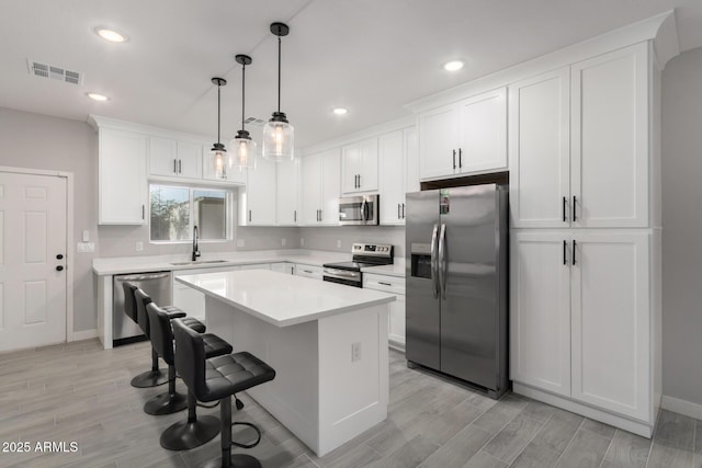 kitchen with stainless steel appliances, sink, pendant lighting, white cabinets, and a center island