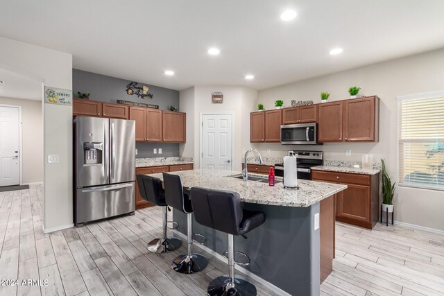 kitchen with appliances with stainless steel finishes, light wood-type flooring, a center island with sink, and a kitchen breakfast bar