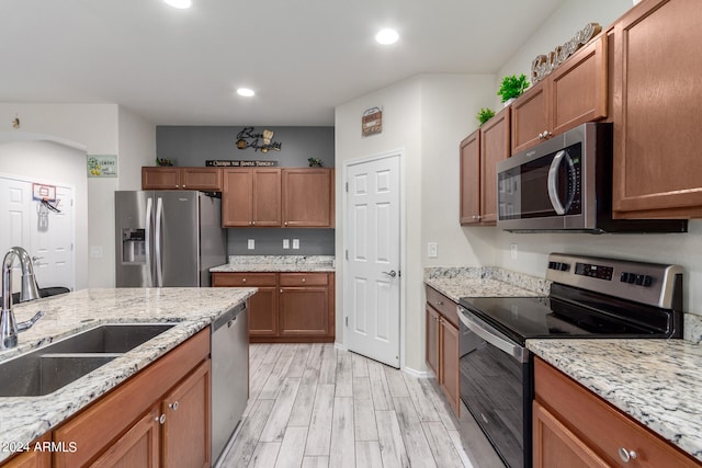 kitchen with light hardwood / wood-style floors, appliances with stainless steel finishes, sink, and light stone counters