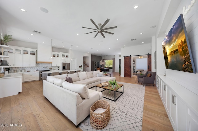 living room with light hardwood / wood-style flooring, a barn door, and ceiling fan