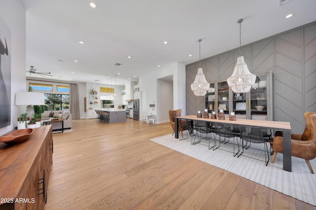 dining area featuring ceiling fan with notable chandelier and light hardwood / wood-style flooring