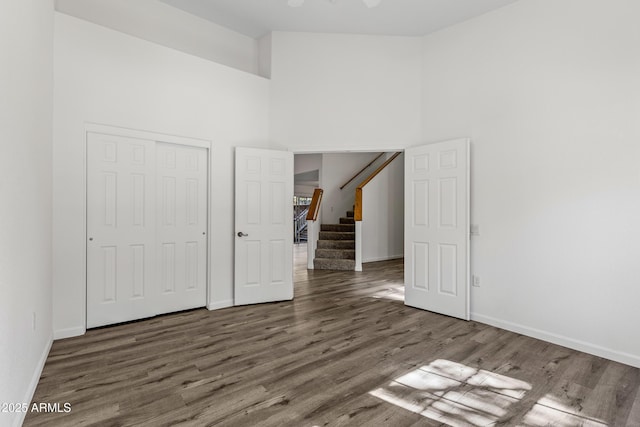 unfurnished bedroom featuring a closet, baseboards, wood finished floors, and a towering ceiling