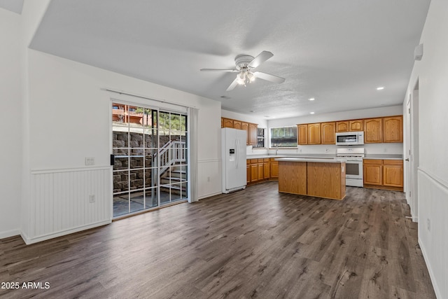 kitchen with white appliances, brown cabinetry, a kitchen island, dark wood finished floors, and light countertops