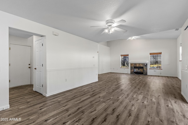 unfurnished living room with visible vents, a tiled fireplace, wainscoting, wood finished floors, and a ceiling fan