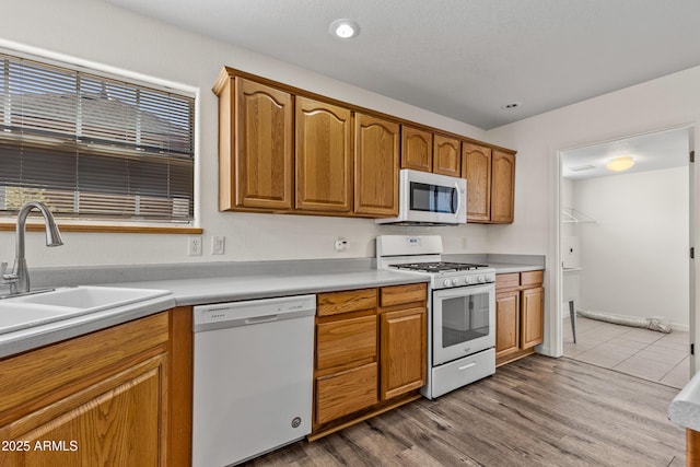 kitchen with white appliances, brown cabinetry, wood finished floors, a sink, and light countertops