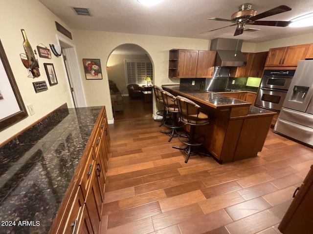 kitchen featuring visible vents, arched walkways, wall chimney exhaust hood, a kitchen breakfast bar, and open shelves