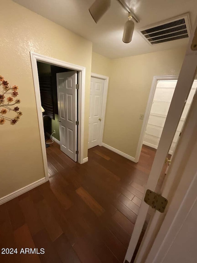 hallway featuring dark wood-type flooring, rail lighting, visible vents, and baseboards