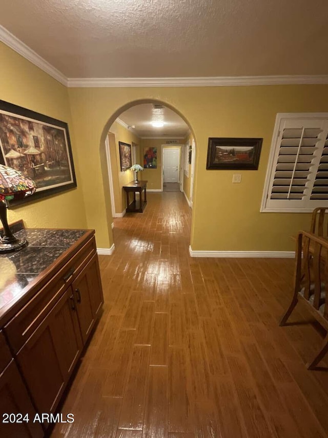 hall featuring crown molding, a textured ceiling, arched walkways, and wood finished floors