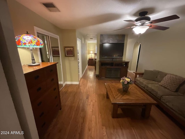 living area featuring a ceiling fan, visible vents, baseboards, and wood finished floors