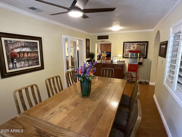 dining space with baseboards, visible vents, arched walkways, a ceiling fan, and crown molding