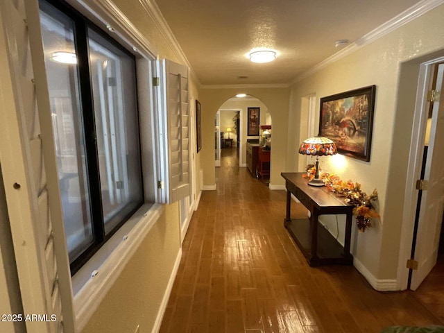 hallway featuring ornamental molding, arched walkways, baseboards, and wood finished floors