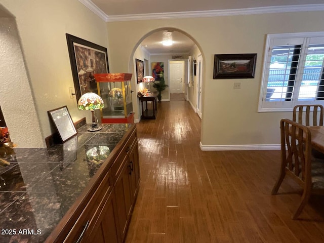 hall featuring arched walkways, baseboards, wood finished floors, and crown molding