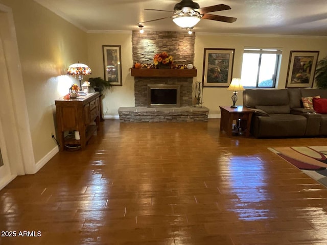 living room with crown molding, wood-type flooring, ceiling fan, a stone fireplace, and baseboards