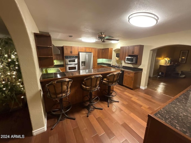 kitchen featuring arched walkways, a peninsula, light wood-style floors, appliances with stainless steel finishes, and dark countertops