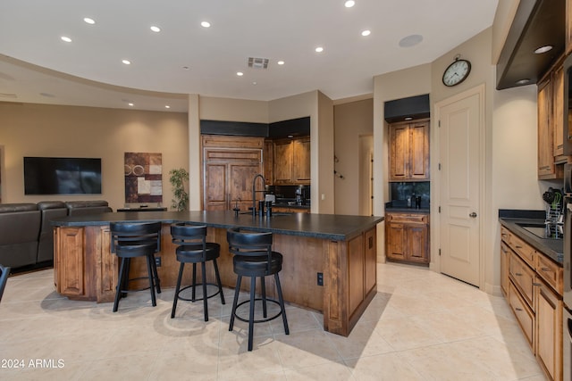 kitchen with a kitchen breakfast bar, a large island with sink, backsplash, and light tile patterned flooring