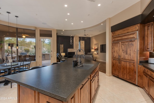 kitchen featuring ceiling fan, sink, light tile patterned floors, decorative light fixtures, and a center island with sink