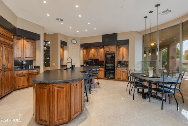 kitchen featuring light tile patterned floors, decorative light fixtures, black appliances, and an island with sink