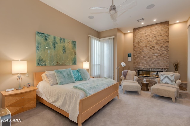 carpeted bedroom featuring ceiling fan and a stone fireplace