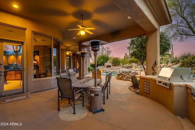 patio terrace at dusk featuring a grill, ceiling fan, and exterior kitchen