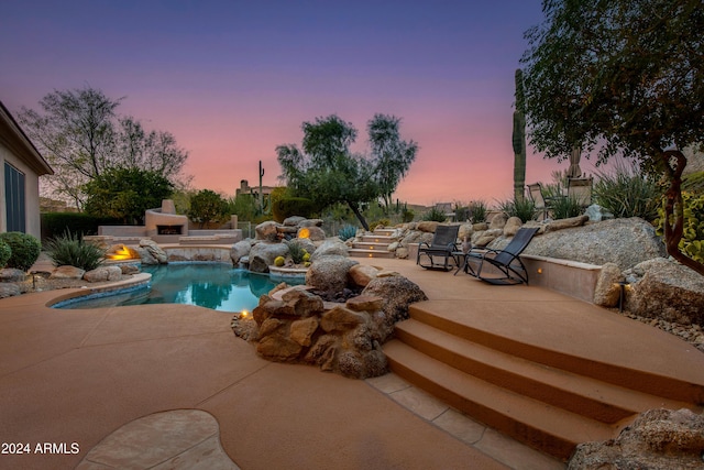 pool at dusk featuring pool water feature, a patio area, and exterior fireplace