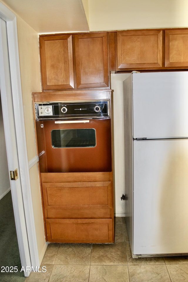 kitchen featuring wall oven, light tile patterned flooring, and white fridge