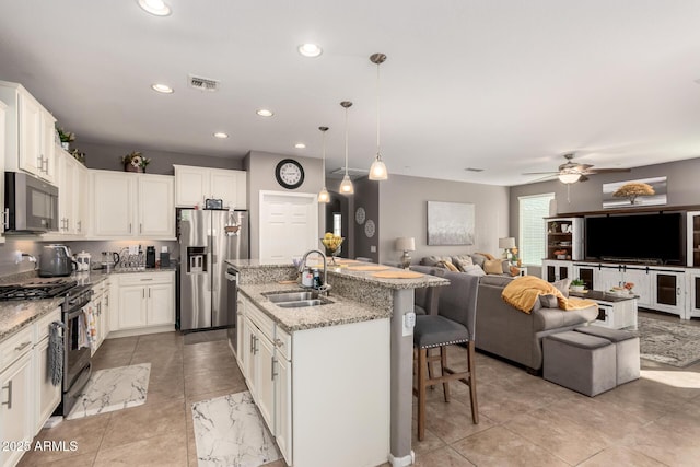 kitchen featuring sink, appliances with stainless steel finishes, white cabinetry, an island with sink, and decorative light fixtures