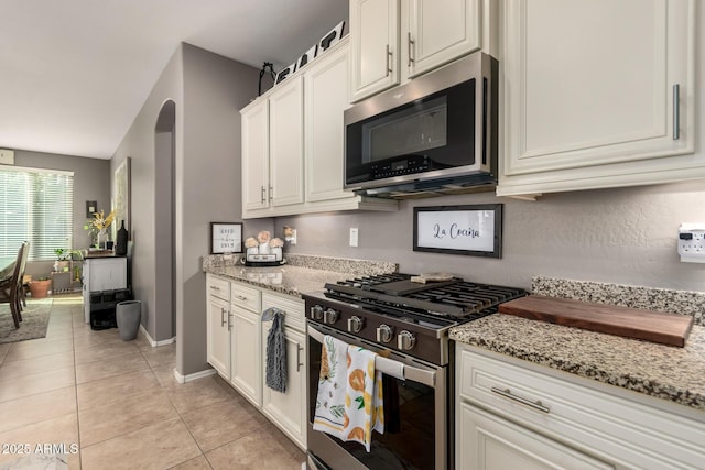 kitchen featuring light tile patterned flooring, light stone countertops, white cabinets, and appliances with stainless steel finishes