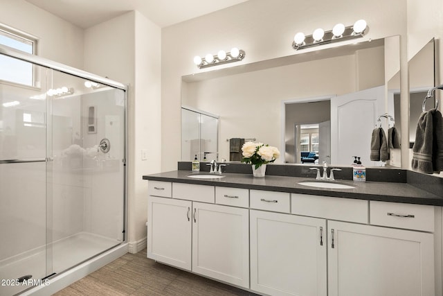 bathroom with a stall shower, wood finished floors, a sink, and double vanity