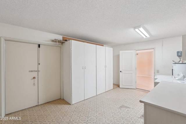 unfurnished bedroom featuring electric water heater, ensuite bath, independent washer and dryer, a textured ceiling, and a closet