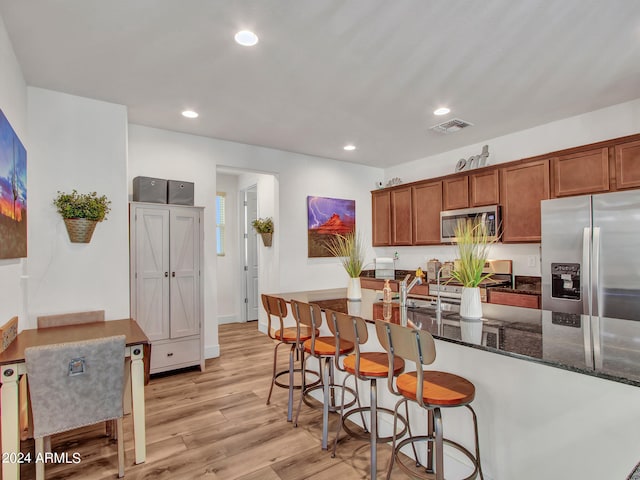 kitchen featuring light hardwood / wood-style flooring, stainless steel appliances, dark stone countertops, and a breakfast bar