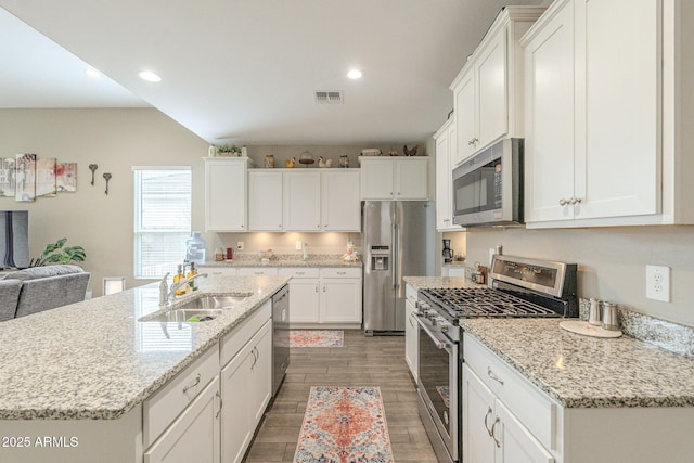 kitchen with wood finish floors, an island with sink, a sink, white cabinets, and appliances with stainless steel finishes