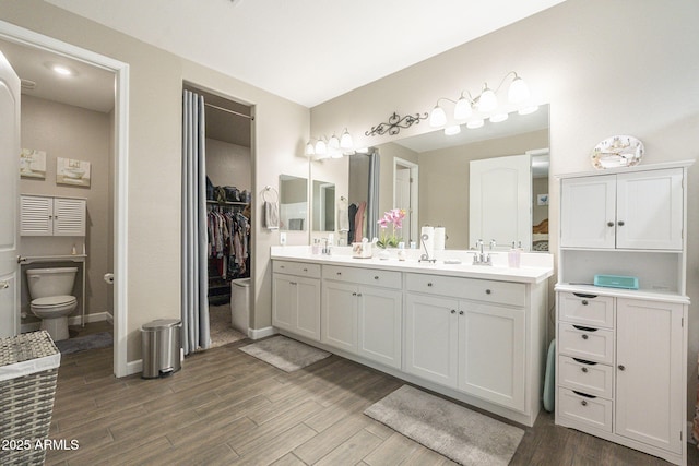 full bath with toilet, a sink, wood finished floors, double vanity, and baseboards