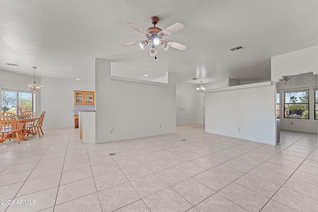 unfurnished living room with ceiling fan with notable chandelier, light tile patterned floors, and plenty of natural light