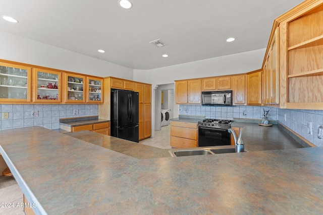 kitchen with kitchen peninsula, black appliances, sink, tasteful backsplash, and washing machine and dryer