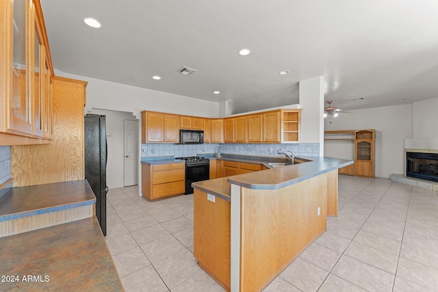 kitchen featuring kitchen peninsula, black appliances, sink, tasteful backsplash, and a tile fireplace