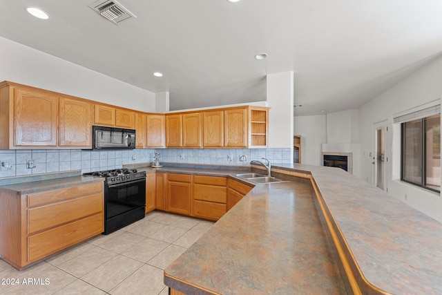 kitchen featuring light tile patterned flooring, a tiled fireplace, sink, black appliances, and tasteful backsplash