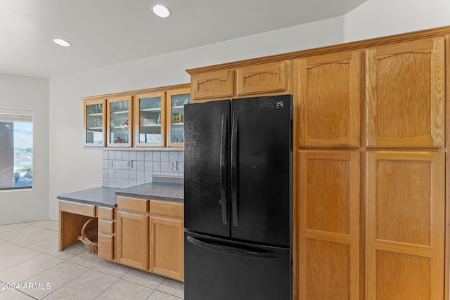 kitchen featuring light tile patterned floors, black fridge, and backsplash